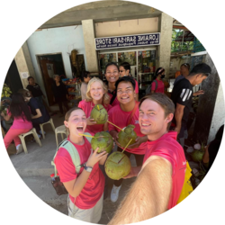 A student missionary is taking a selfie with a group. They are all holding fruit in their hands.